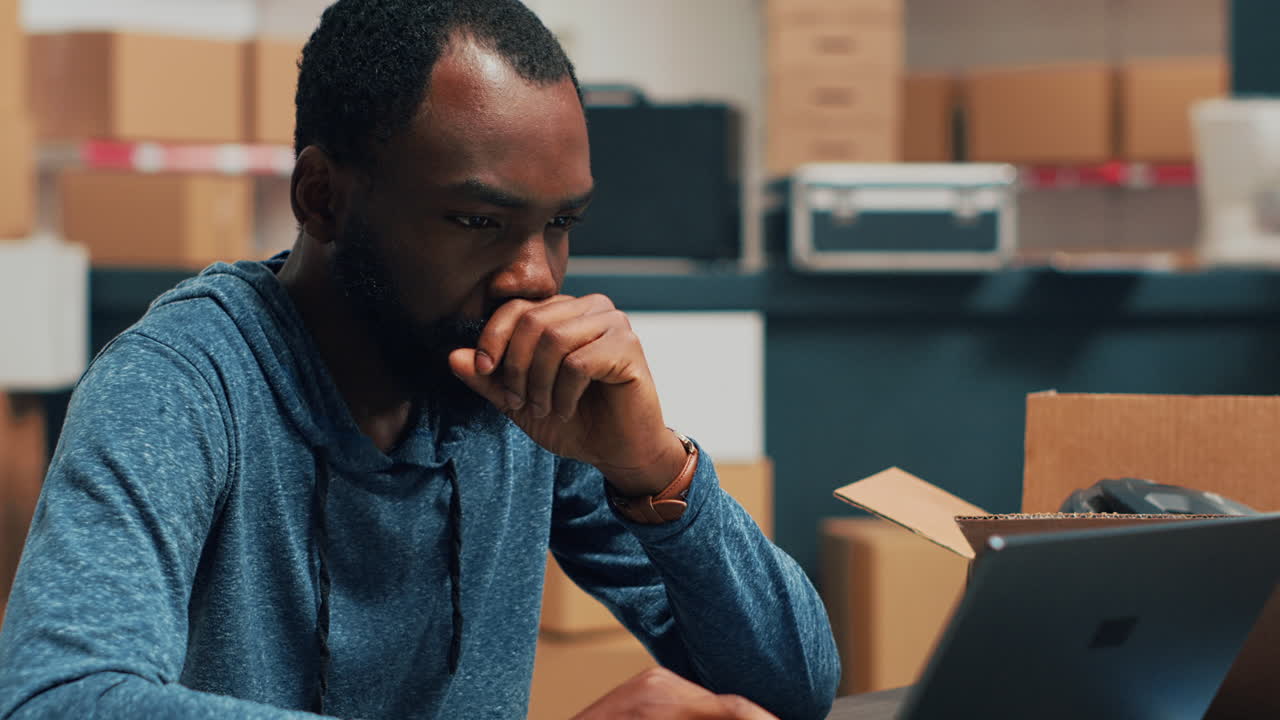 Man working on laptop in warehouse with boxes