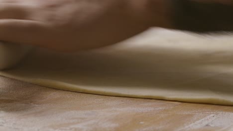 hands of man using rolling pin to roll dough on kitchen table