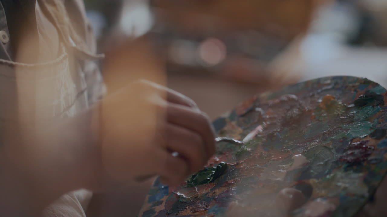Mani di artista che mescolano colori a olio con una spatola.