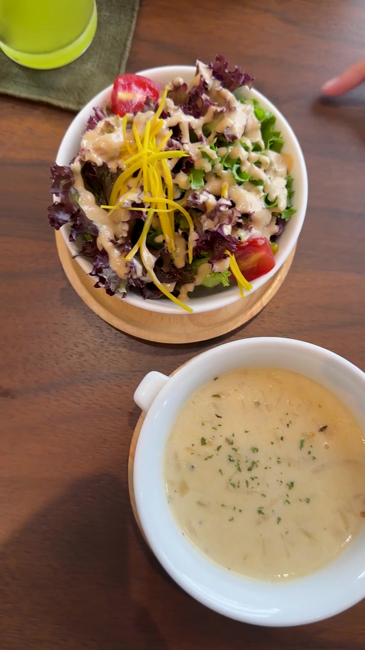 Vista superior de salada e sopa creme dispostas em mesa de madeira sob luz natural brilhante.