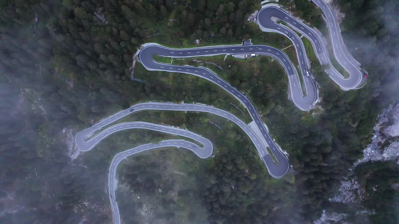 Top down drone shot rotating above a serpentine road, in the foggy alps