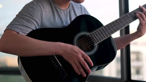 man playing acoustic guitar by window