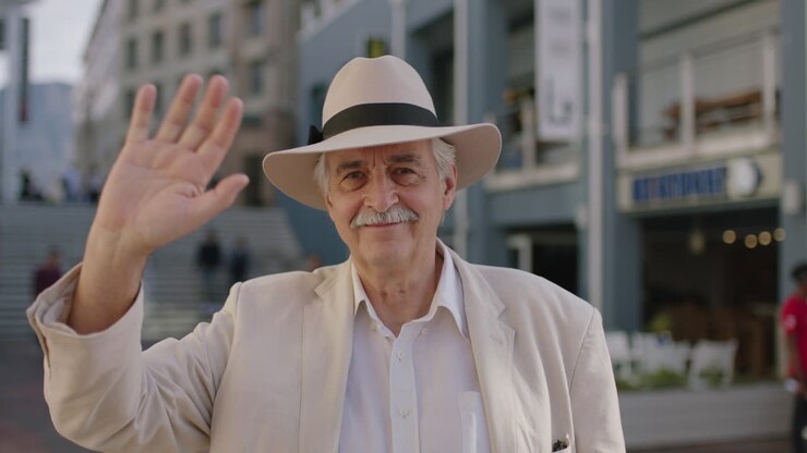 ritratto di un uomo anziano elegante, un turista sorridente, felice, guardando la fotocamera, agitando la mano, godendosi un viaggio di vacanza in città