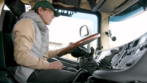 side view of older worker wearing cap and vest driving a truck in a logistics park 4