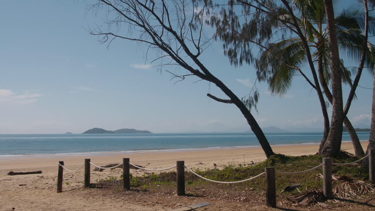 An island in the background of a beach with trees, sand and a wooden fence in the foreground