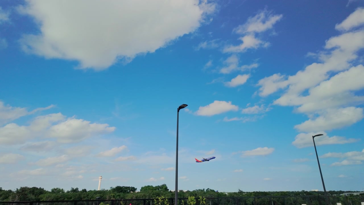 Un aereo di linea sale ripidamente in un cielo blu vivido costellato di nuvole bianche, sopra i lampioni di un parcheggio aeroportuale a Cancun, sulla costa caraibica del Messico, riportando a casa i vacanzieri.