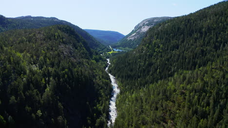Flying-over-river-winding-through-evergreen-forest-mountains-in-Norway