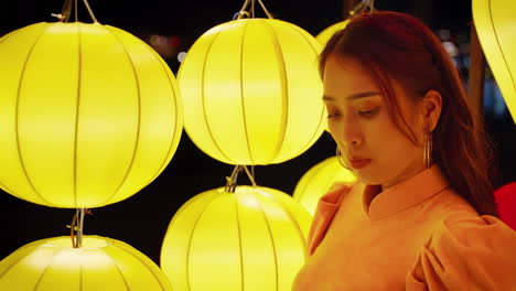 una mujer de naranja, ao dai, admira las linternas amarillas por la noche en hoi an.