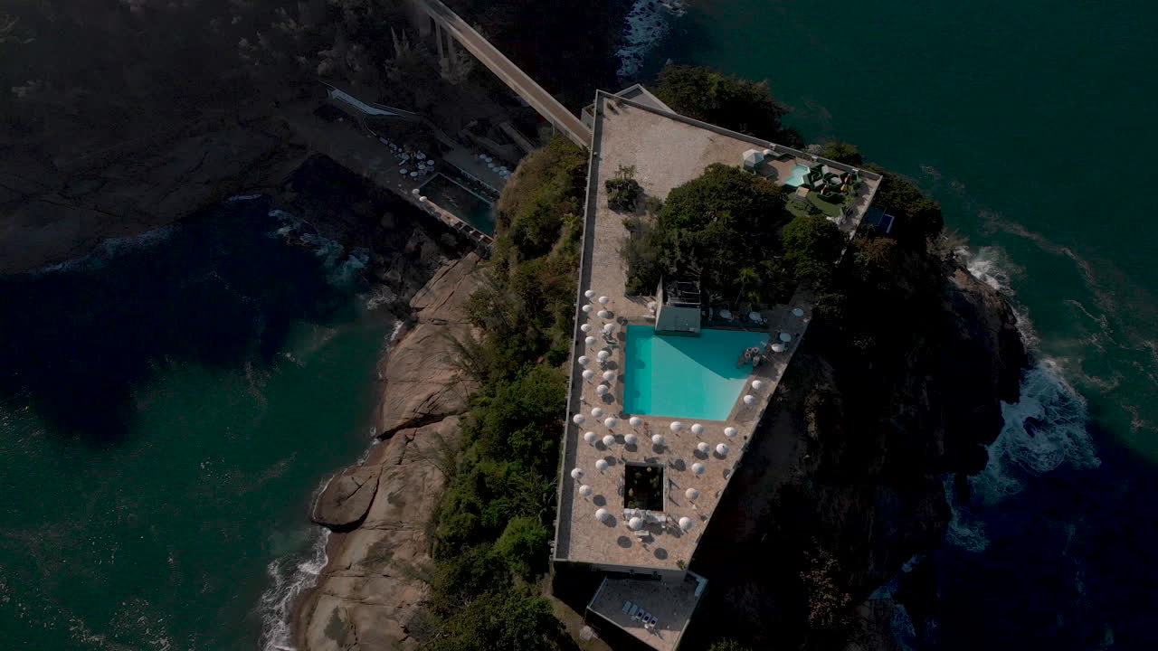 vista aérea de arriba hacia abajo de una construcción recreativa en una pequeña isla en la costa de río de janeiro vista desde arriba al atardecer con sombrillas que dan sombra alrededor de la piscina