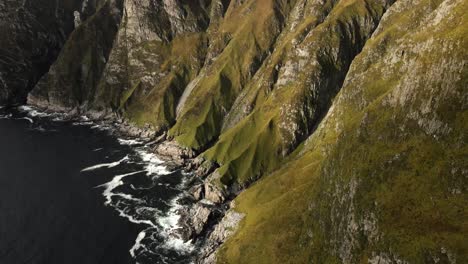 Aerial-top-down-shot-of-idyllic-green-mountains-with-rocky-coastline-with-Atlantic-Ocean-at-sunset