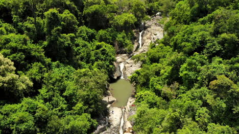 People-swimming-on-a-lake-in-rocks-and-waterfall,-with-a-road-and-ocean-on-the-background