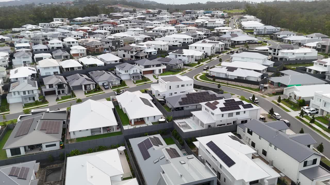 Drone ascends over contemporary suburban homes, revealing dense residential layout under overcast daylight