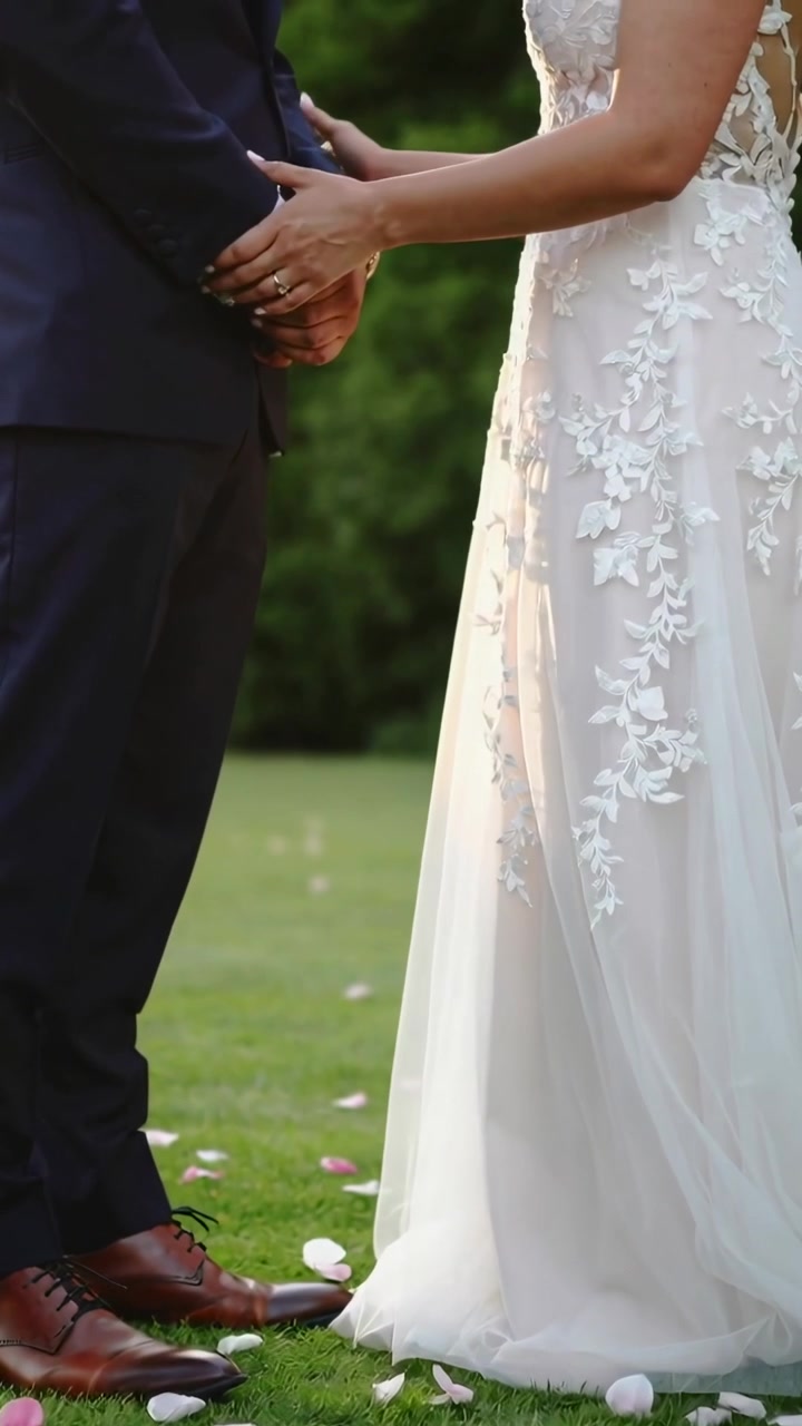 Vertical video: Reaching bride in lace gown after clasp fixing cuff holding waist on lawn for vows