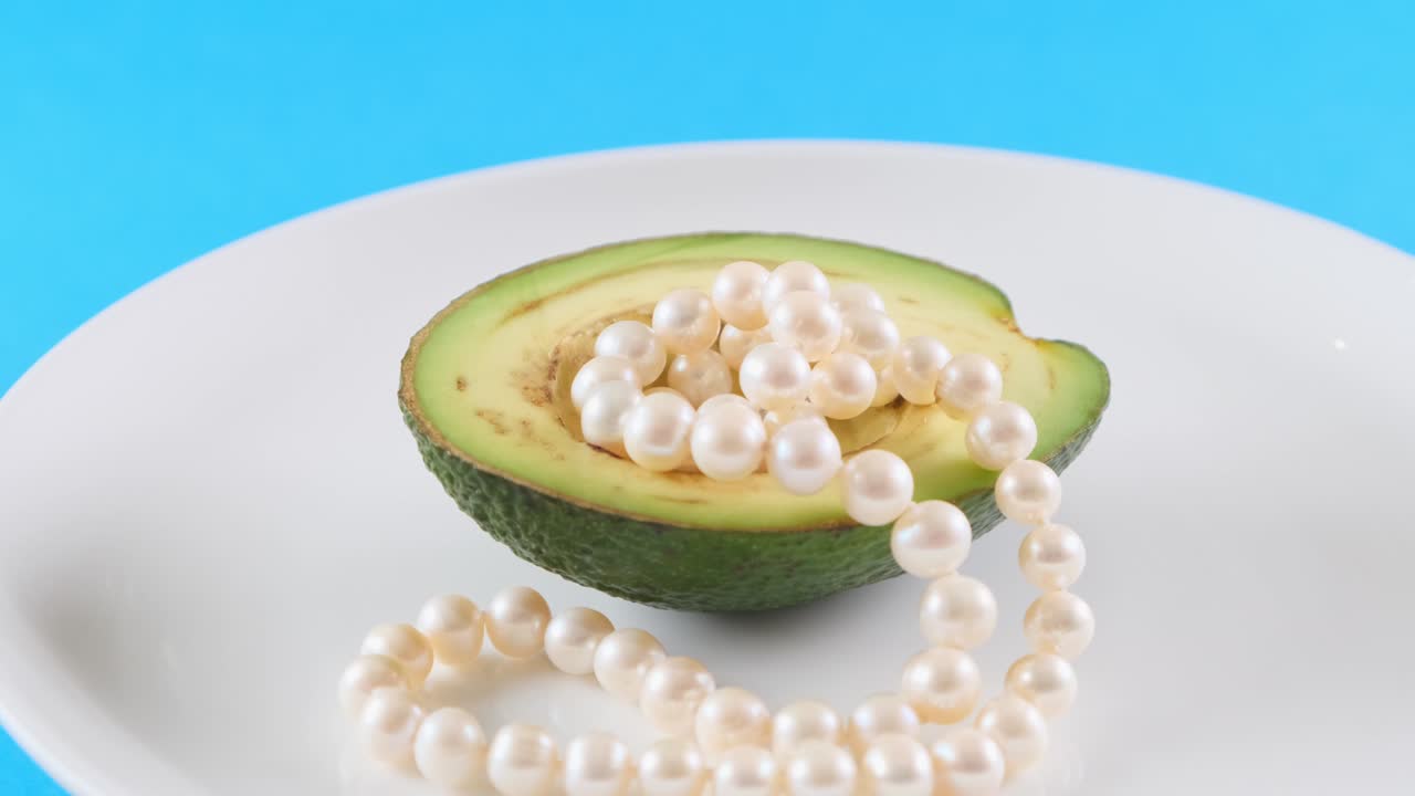 파란색 배경에 색 접시에 진주와 함께 아보카도 반. 패션 음식 디자인