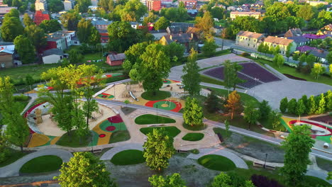 Toma-Aérea-De-Un-Vibrante-Parque-Comunitario-Con-áreas-De-Juegos-Infantiles-Y-Exuberante-Vegetación-Durante-La-Puesta-De-Sol