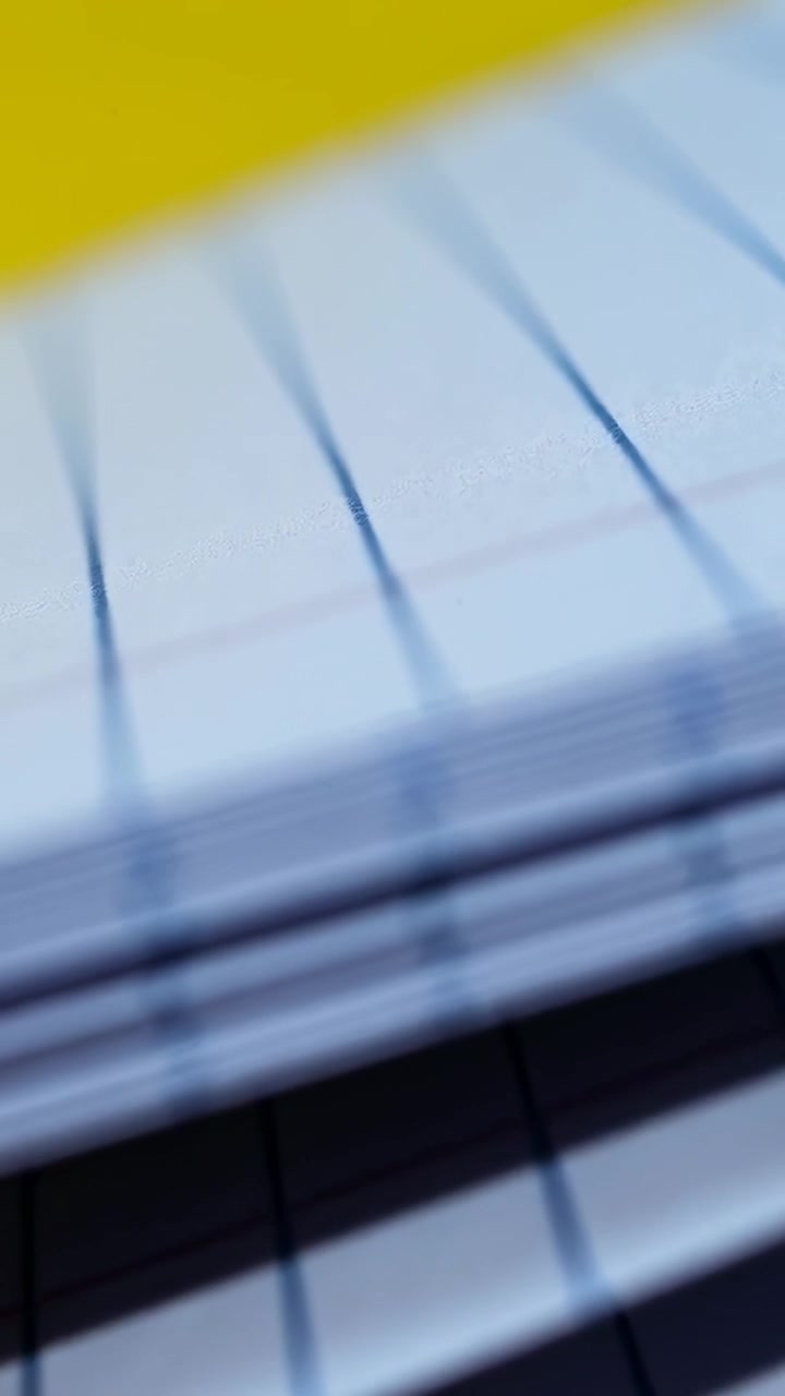 Vertical video: Sliding camera revealing ruled sheets on desk, showing yellow back and blue lines
