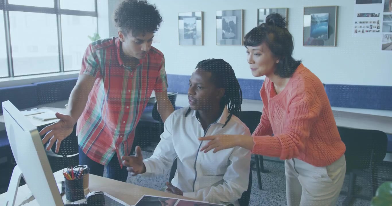 Seated man clicking mouse while team pointing at prints and monitor, selecting visuals for design