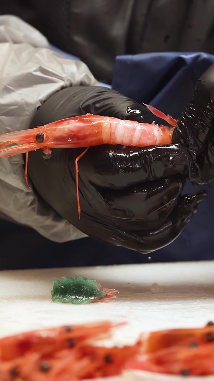Close-up of a chef peeling raw prawns for sushi preparation in a Tokyo kitchen.