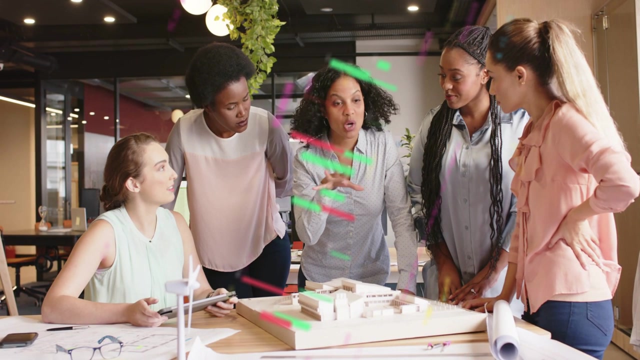 Design team of five women reviewing model, lead stepping gesturing, green red streaks marking plans