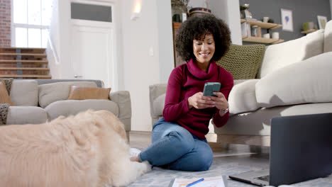 Mujer-Birracial-Feliz-Con-Perro-Golden-Retriever-Usando-Laptop-Y-Teléfono-Inteligente-En-Casa,-Cámara-Lenta