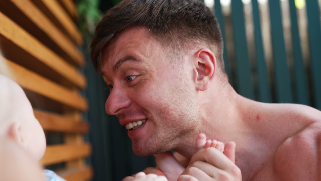 Caucasian father playing with his cute infant. Happy dad smiling to a baby and puts kid's feet on the face. Close up.