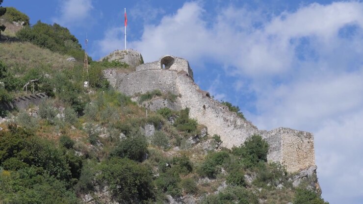 Mura di fortificazione e bastione del Castello di Berat su una ripida collina rocciosa a Berat, in Albania, con la bandiera nazionale su un pennone sopra i bastioni sotto un cielo parzialmente nuvoloso