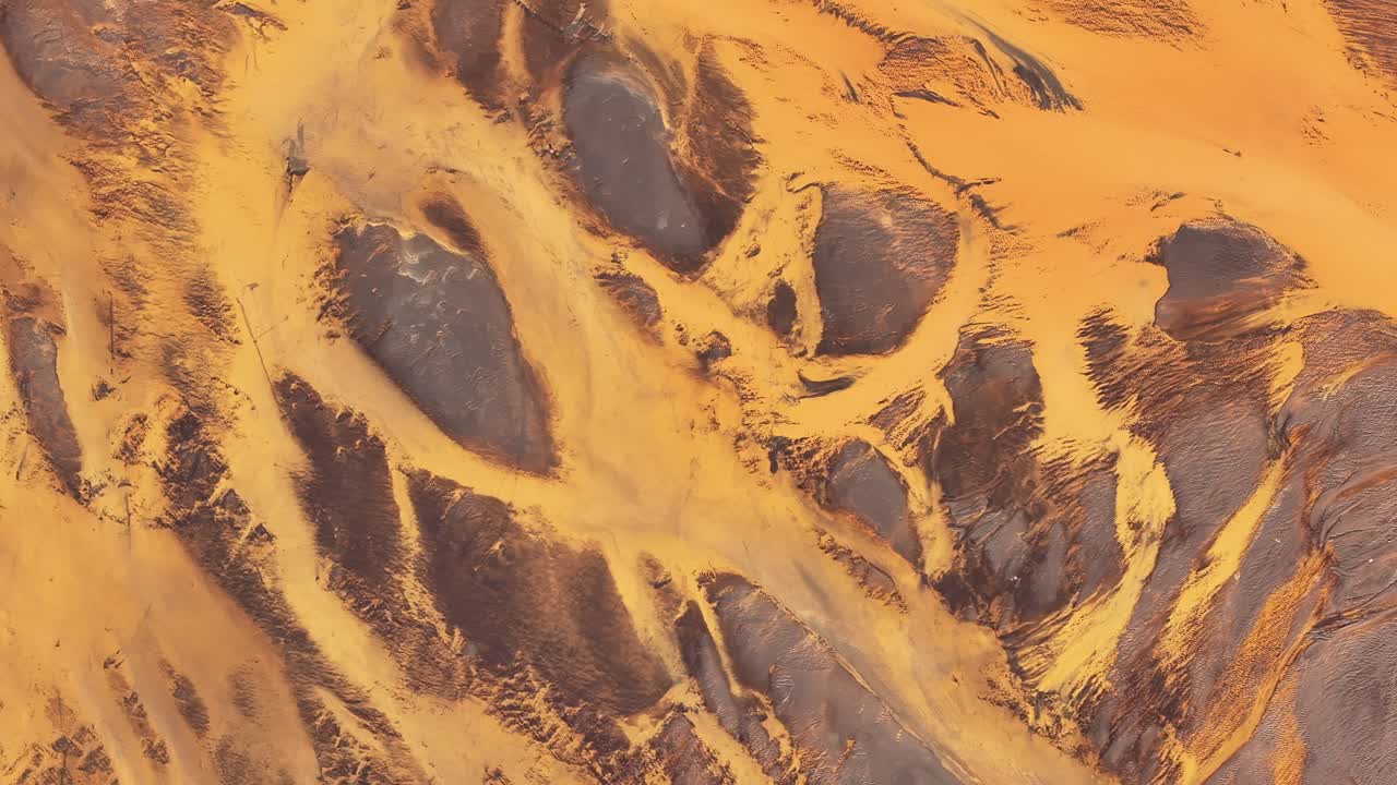 Abstract drone view over Þjórsá river delta in Iceland, golden volcanic sediment and braided channels form surreal natural patterns.