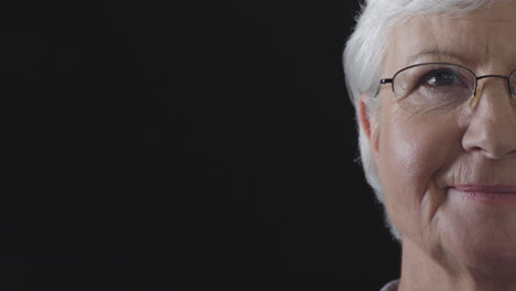 retrato de la mitad de la cara de una anciana feliz sonriendo con satisfacción mirando a la cámara con gafas aisladas en un fondo negro