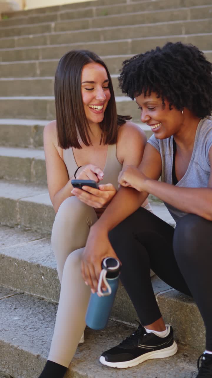Two Happy Friends Sitting on Stairs and Looking at a Smartphone