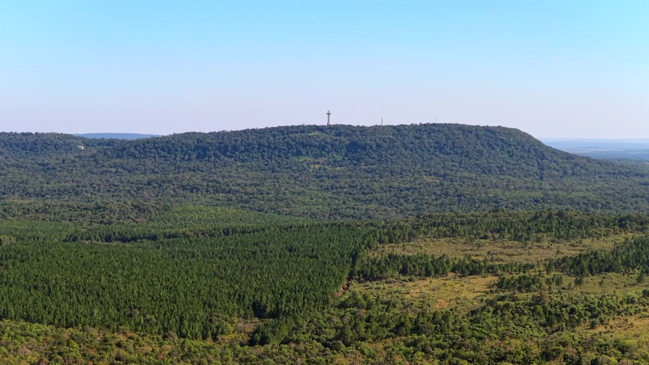 Cerro Santa Ana rises above extensive commercial pine plantations with the Santa Ana Cross visible on the ridge in Misiones, Argentina, forwaed flyover