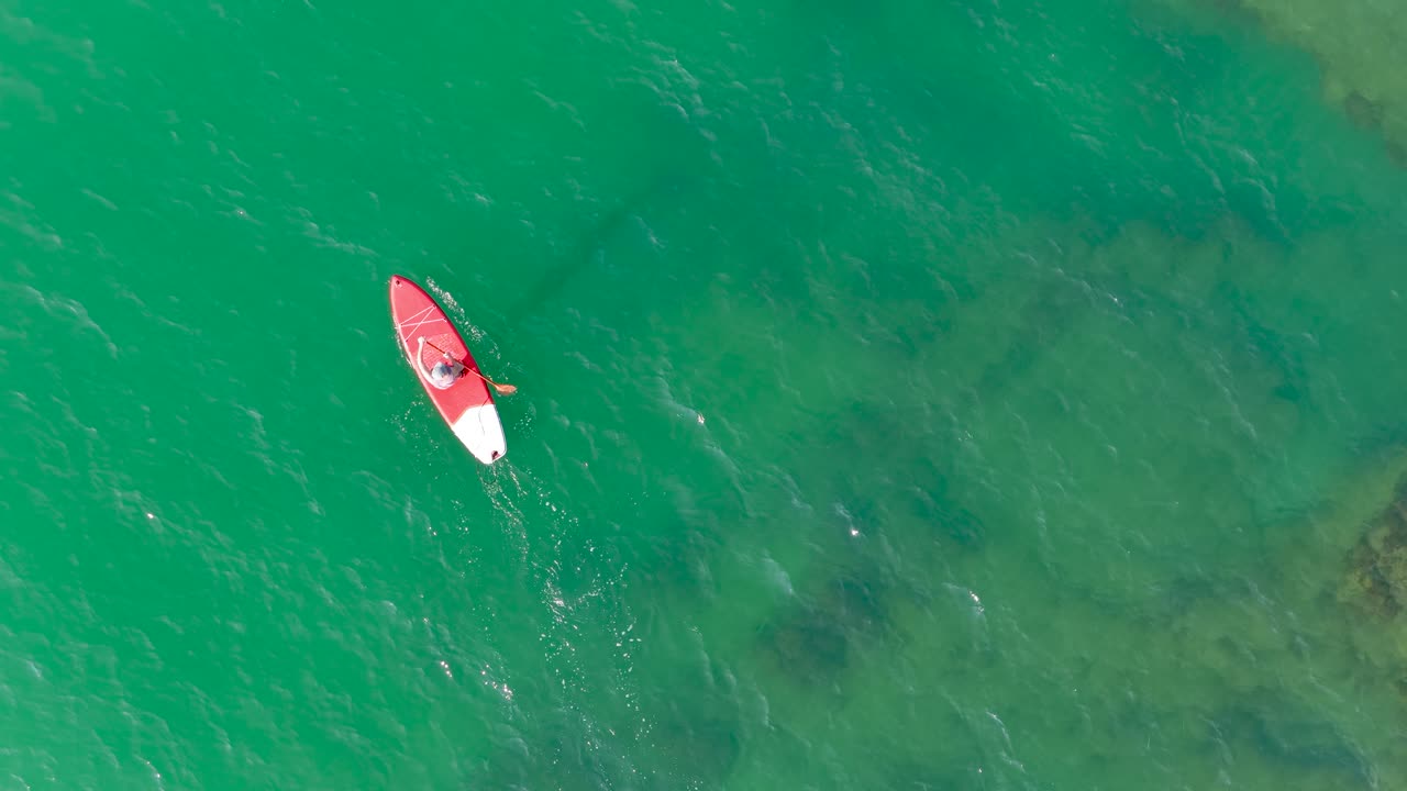Lifeguard paddling on red paddle board in emerald green water