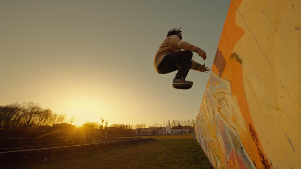 Uomo che salta oltre un muro graffitato al tramonto