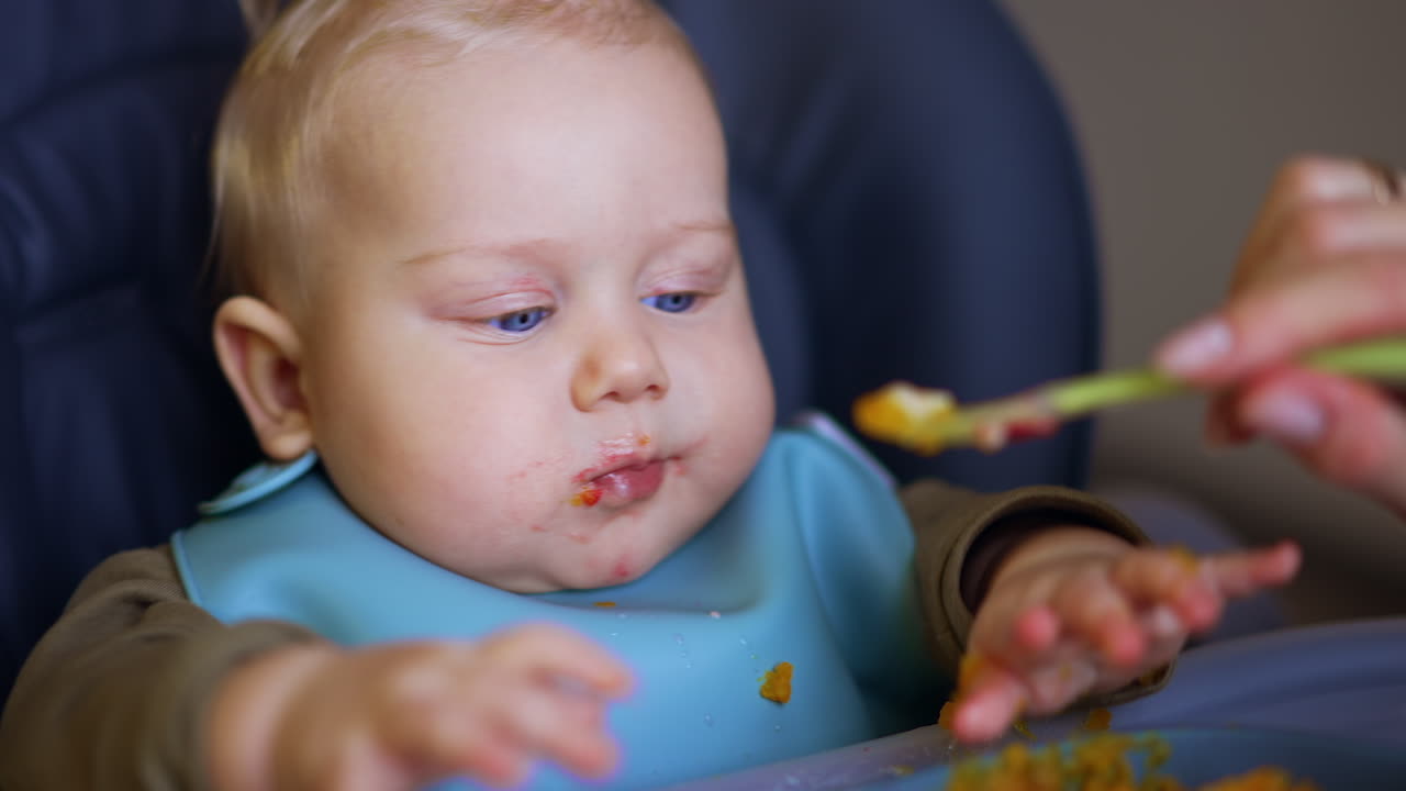 Serious Caucasian baby boy having meals. Healthy food for a little child at home. Close up.