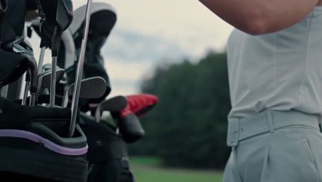 las manos de la mujer sostienen palos y equipos de golf en el campo. golfista activo usando bolsa de putter.