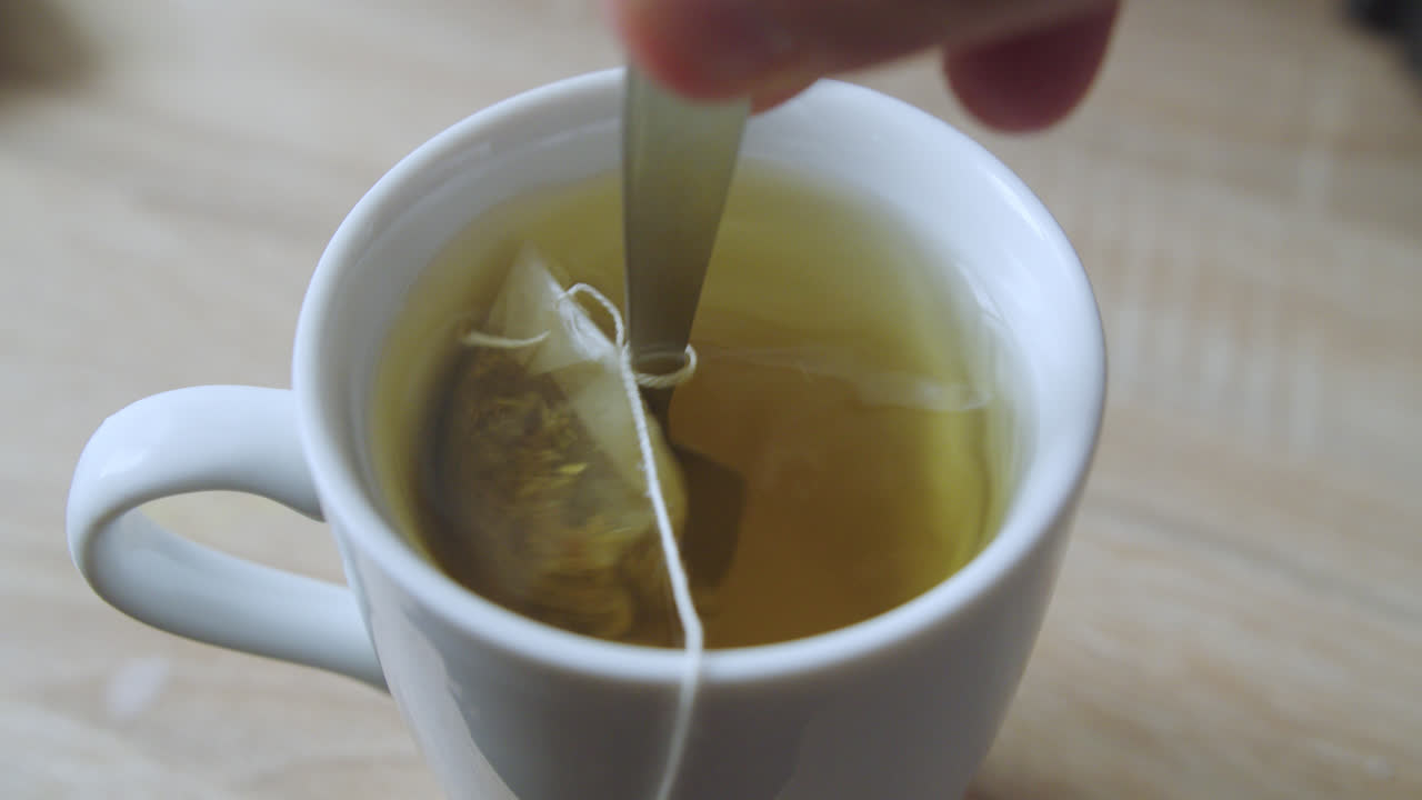 Beautiful close up slow motion shot of a white cup with hot water and chamomile while stirring with a small spoon to mix it with sugar