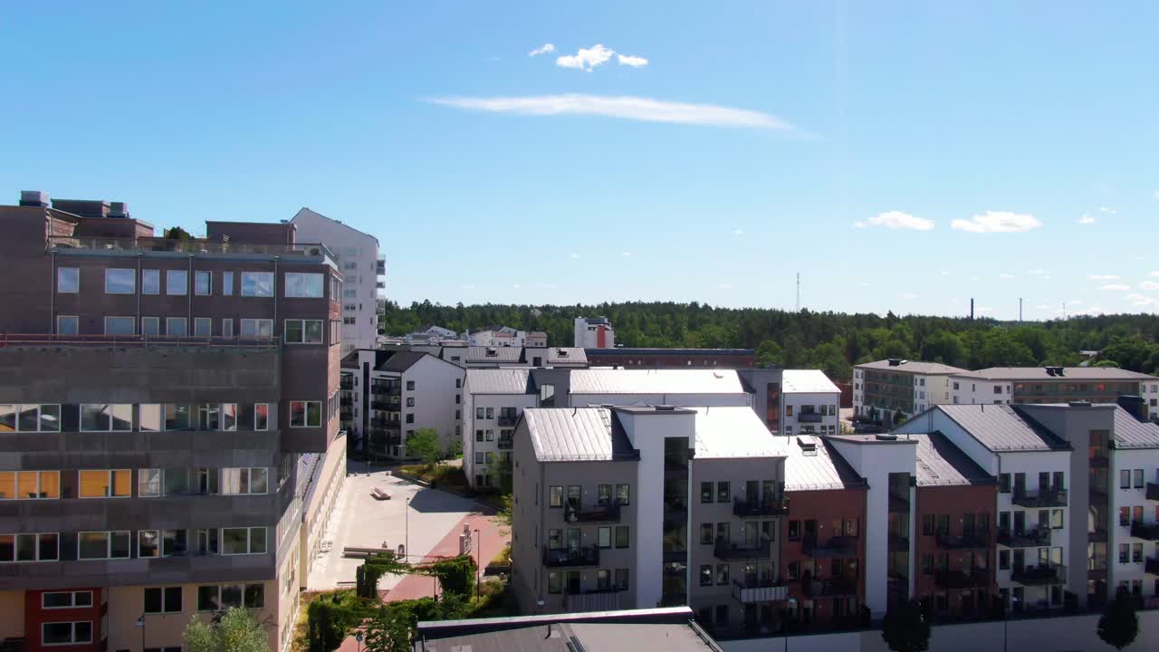 Fantastisk dronebillede af moderne lejlighedsbygninger med varieret arkitektur og grøn horisont i Gustavsberg under en klar, blå himmel. Perfekt til skandinaviske stockbilleder.