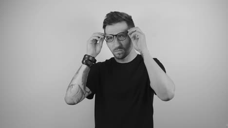 slow motion footage of a man with tattoos putting on glasses to enhance his vision and squints at the camera because of bad eyesight