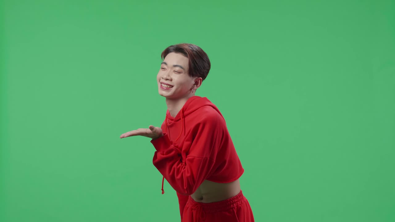 Side View Of A Smiling Asian Transgender Male Blowing Kisses To A Camera In The Green Screen Studio