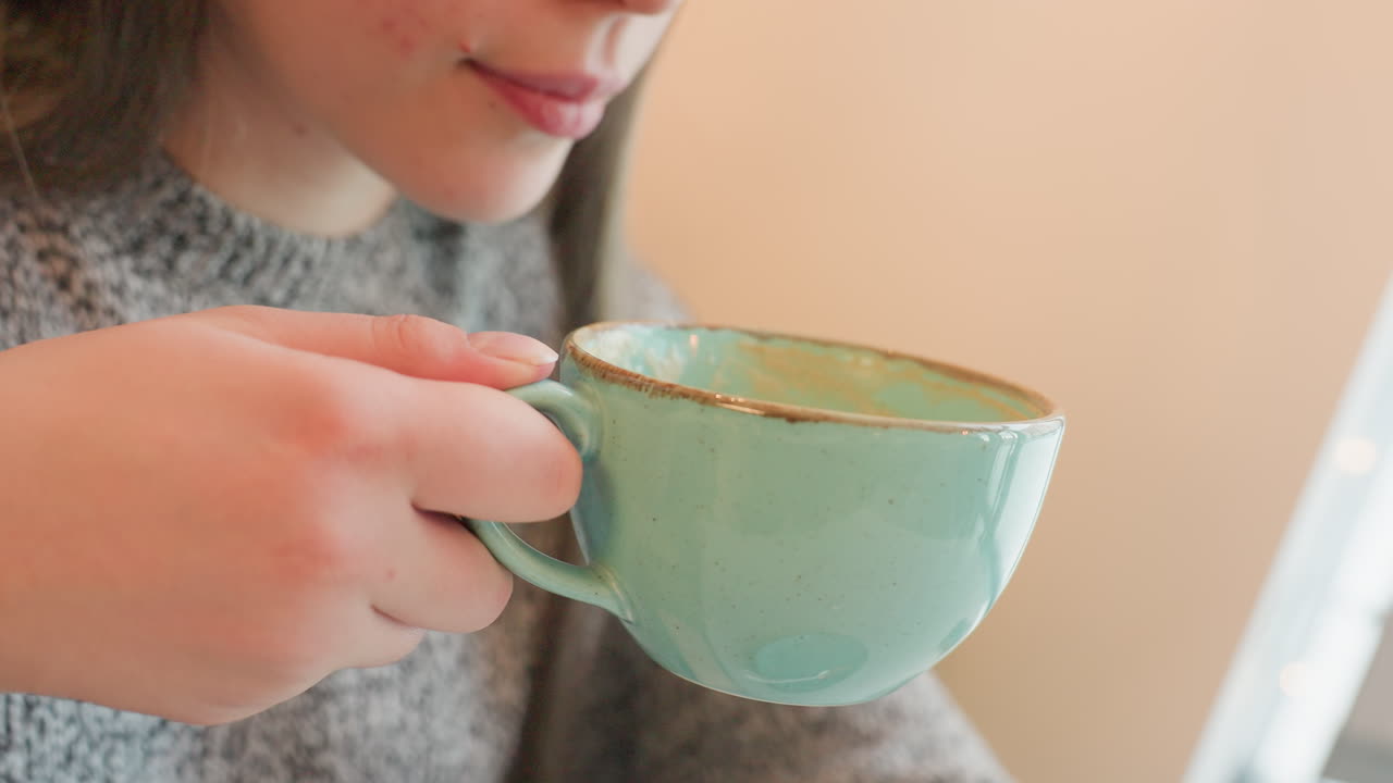 Beautiful lady in eatery sipping hot chocolate drink from turquoise cup with visible enjoyment on face expression cozy indoor setting warm atmosphere casual attire relaxing during break time