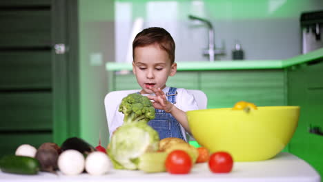 kid making a veggie meal. a young child sits at a table, examining broccoli while surrounded by various fresh vegetables in a bright kitchen