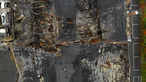 Aerial-view-of-burned-down-building-after-devastating-fire,-zooming-out-shot