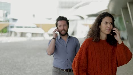 hombre y mujer sonrientes hablando por teléfonos celulares al aire libre