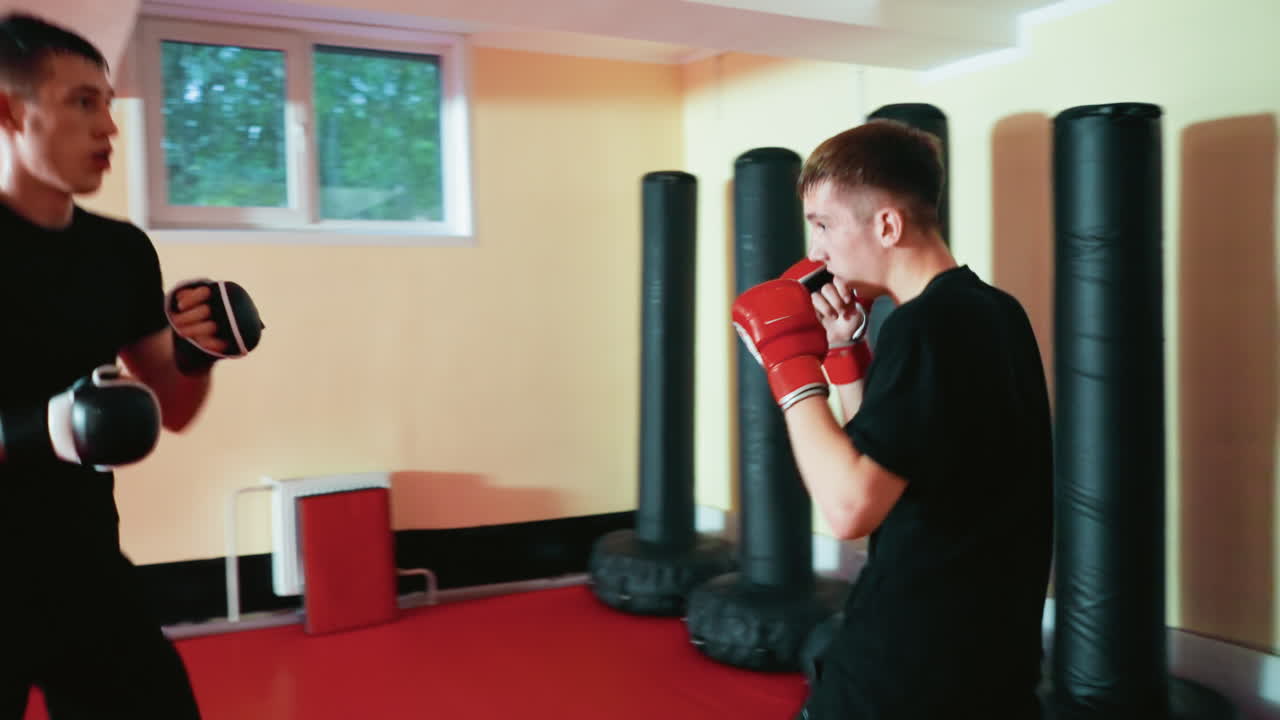 Boxers engaged in punching session on red mat gym floor, delivering straight punch while opponent leans back in defense, showcasing strength, focus, training intensity, and combat movement