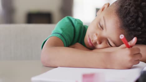 Happy-african-american-boy-sitting-at-table,-doing-homework-and-sleeping