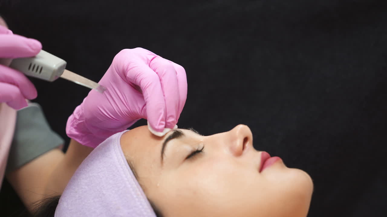 Female cosmetologist using ultrasonic scrubber on client's face. Professional ultrasonic equipment.