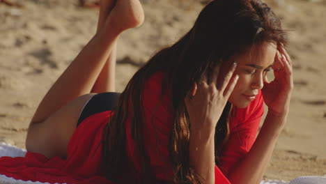 Una-Joven-Descansando-En-Una-Playa-De-Arena-Dorada-Con-Un-Cálido-Sol-En-La-Cara-Se-Pone-Gafas-De-Sol,-Teleobjetivo-De-Tiro-Medio