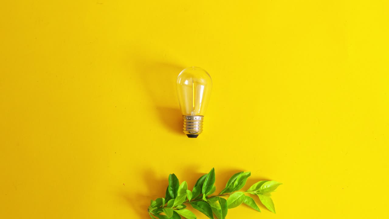 Top view of light bulb and green leaves on vibrant yellow background