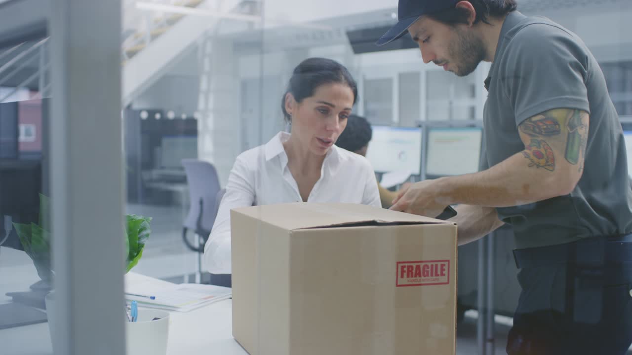 el repartidor entra en la oficina corporativa, entrega el paquete a una hermosa mujer de negocios, ella firma su firma en la tableta.