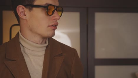 young cheerful man in polarized sunglasses getting ready to go out, puts on coat and smiles at the camera