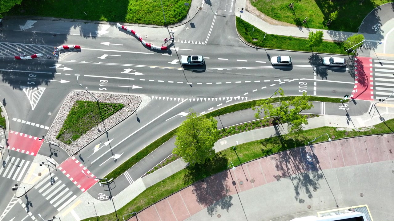 Birds eye view of a modern urban road junction featuring cars, bus lanes, and bicycle paths. High angle shot capturing city infrastructure and transportation flow.